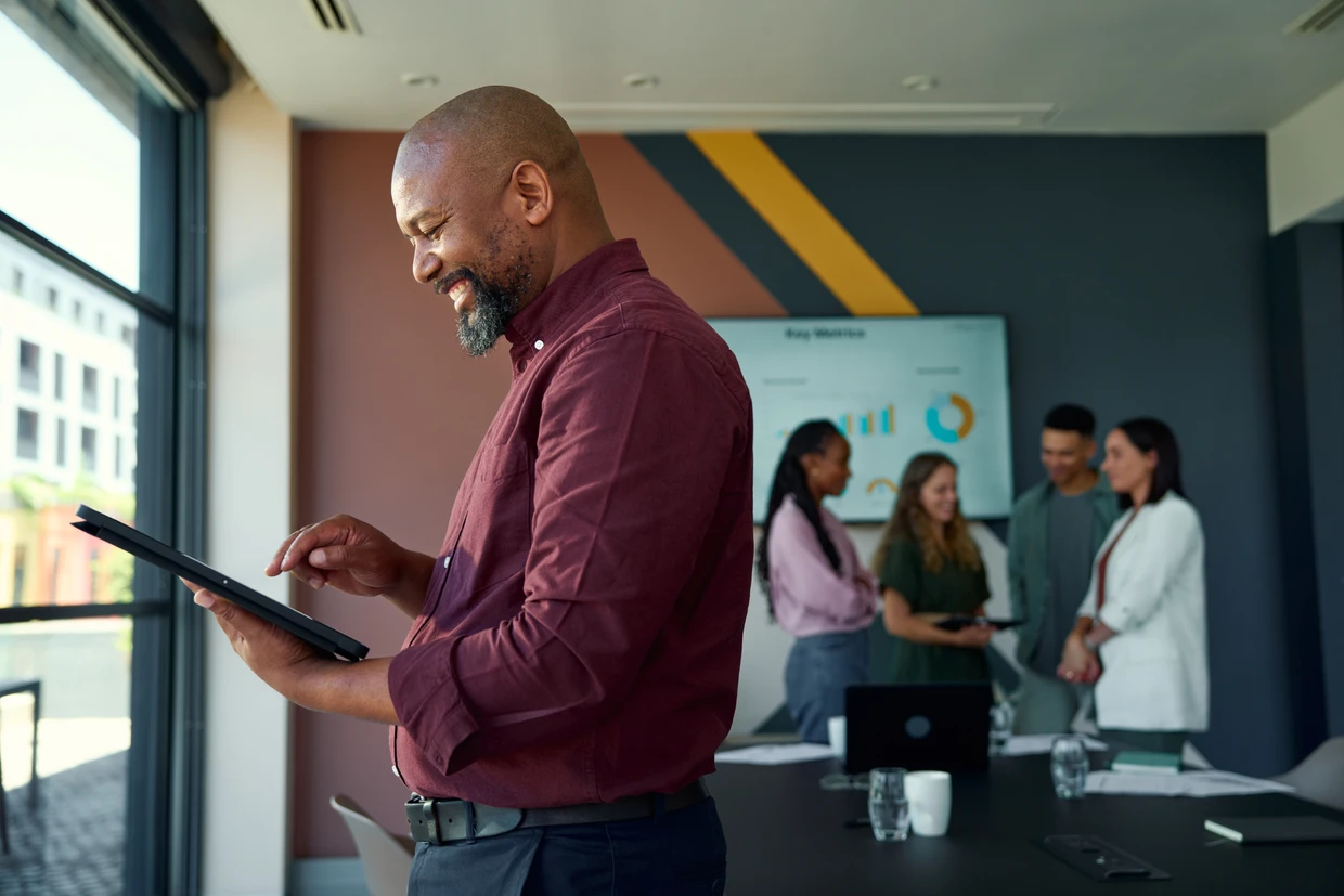 Man using a tablet while colleagues meet in an office