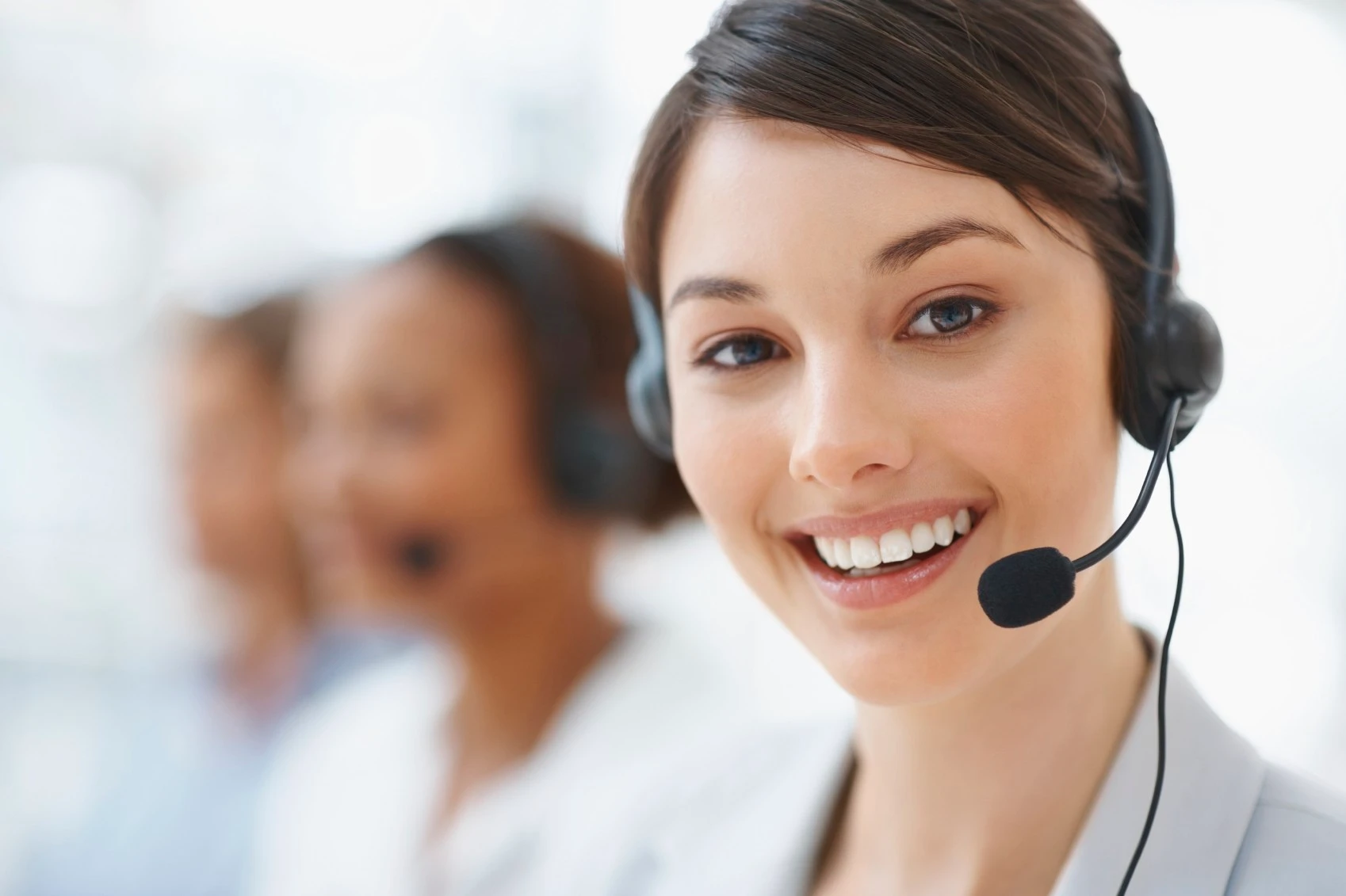 Support specialist wearing a headset, with coworkers behind her
